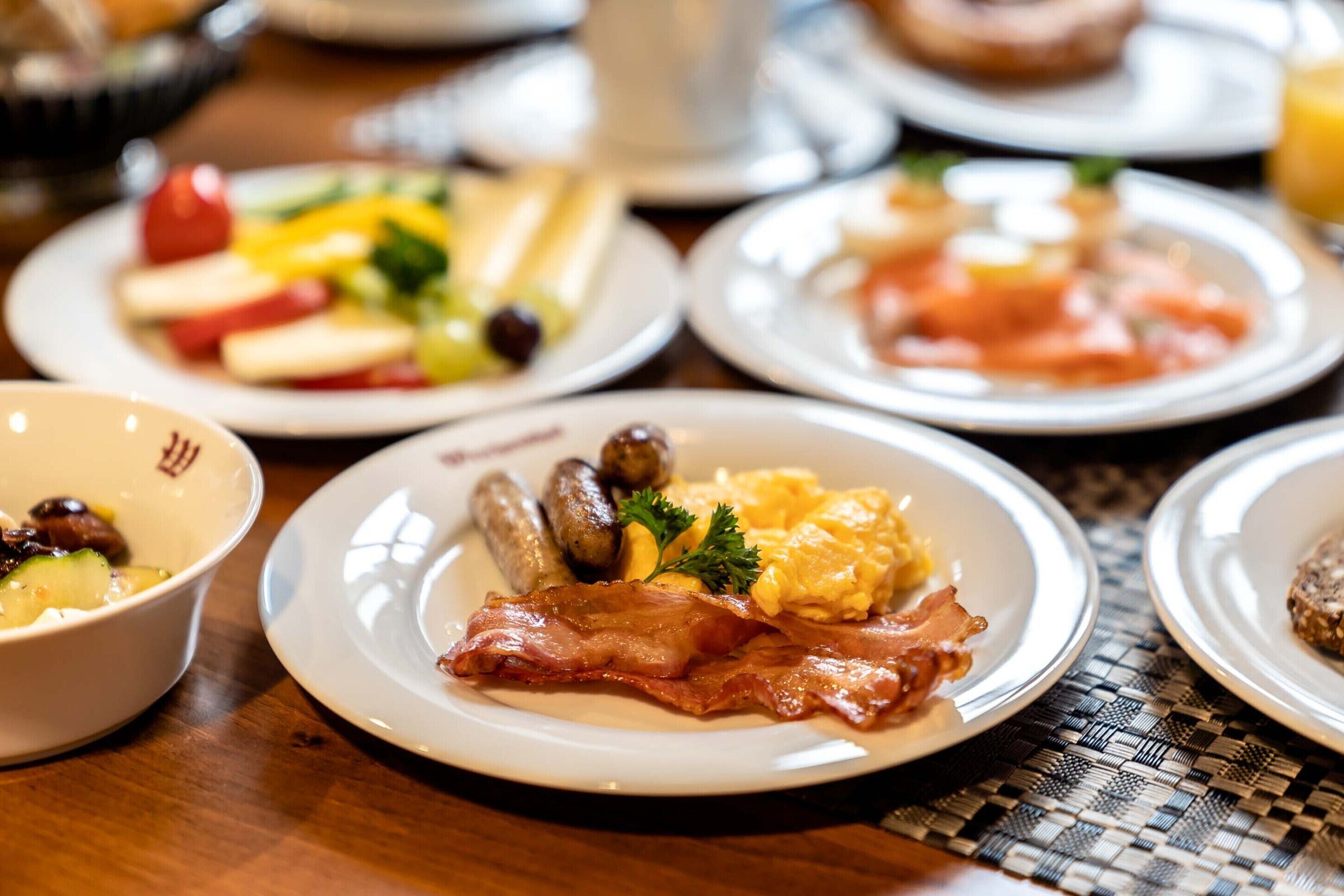 A breakfast setting with plates of eggs, sausages, and bacon.