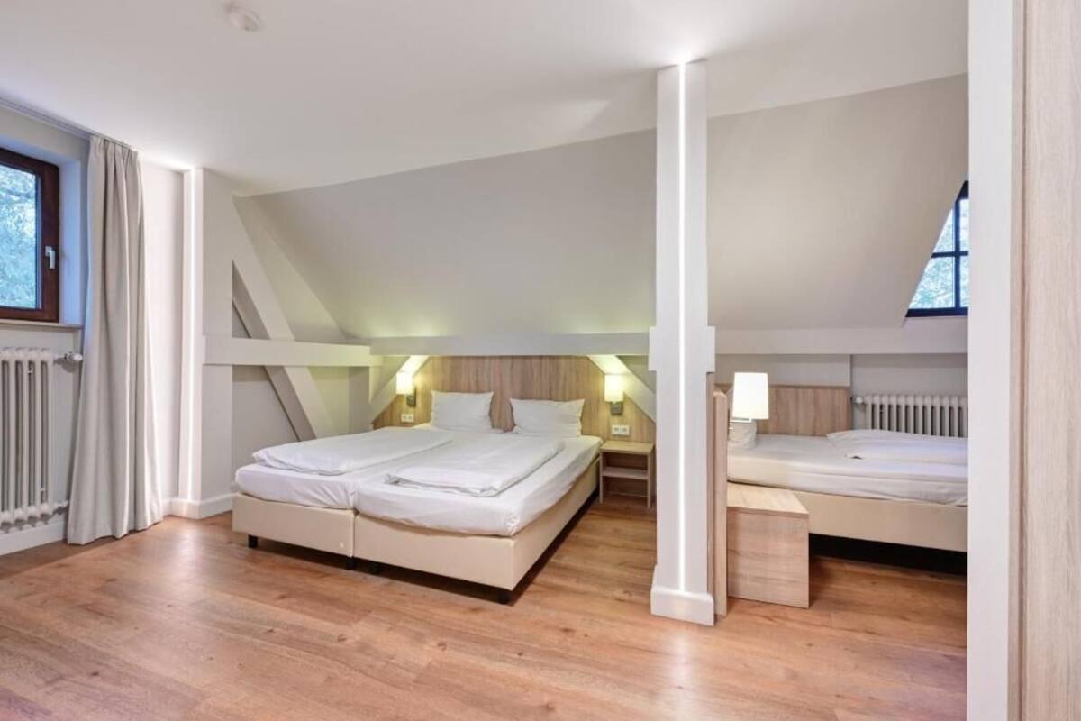 Una camera da letto con un letto grande, un letto più piccolo e una scrivania. Ci sono due comodini con lampade. Il pavimento è in legno e il soffitto è a falde.