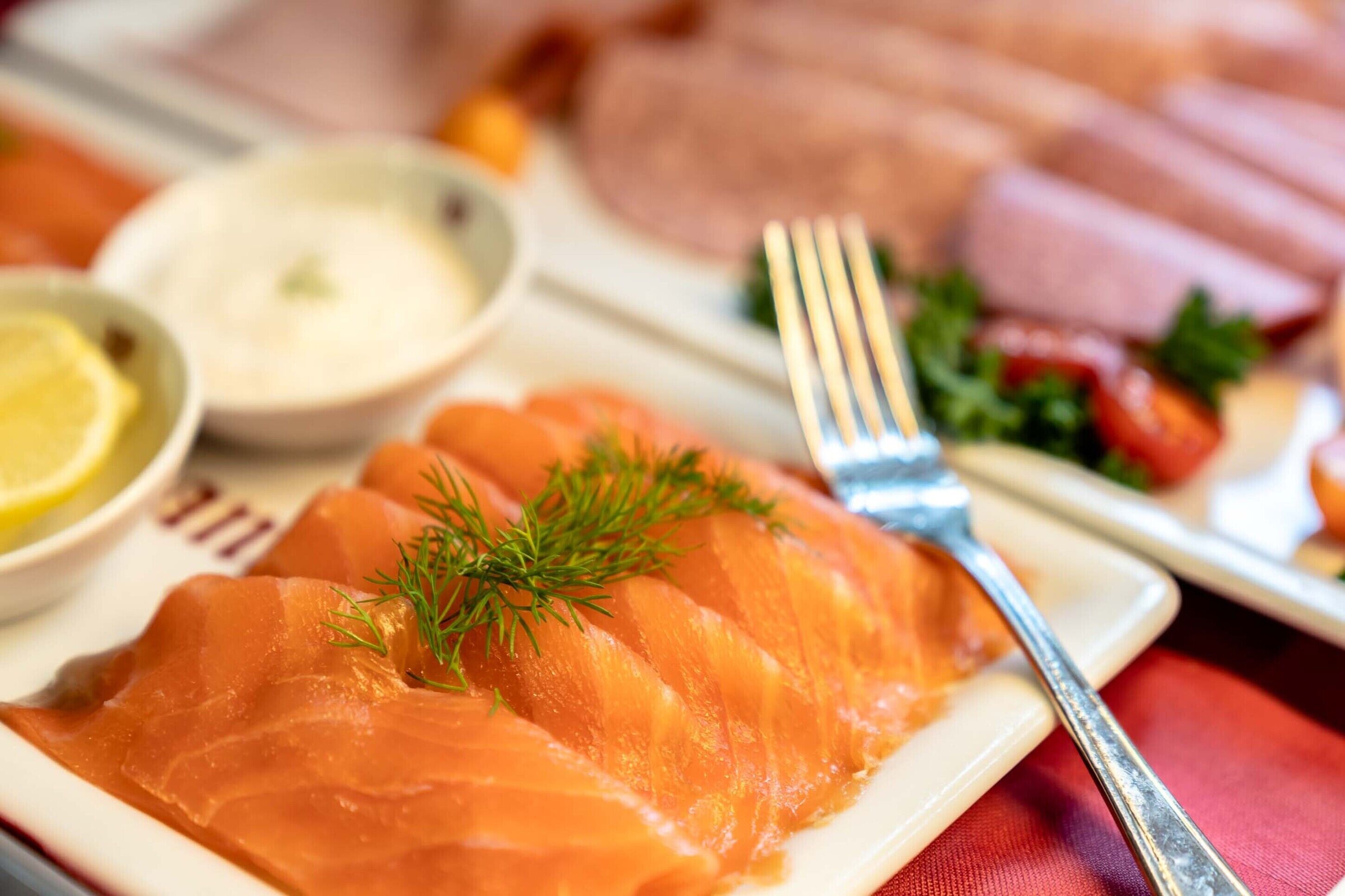 Un plato de salmón ahumado decorado con eneldo, acompañado de un tenedor y recipientes pequeños con salsas.