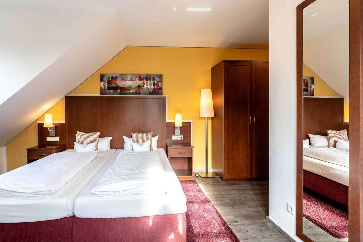 Una camera d'albergo con due letti, un armadio in legno, un quadro appeso e uno specchio.