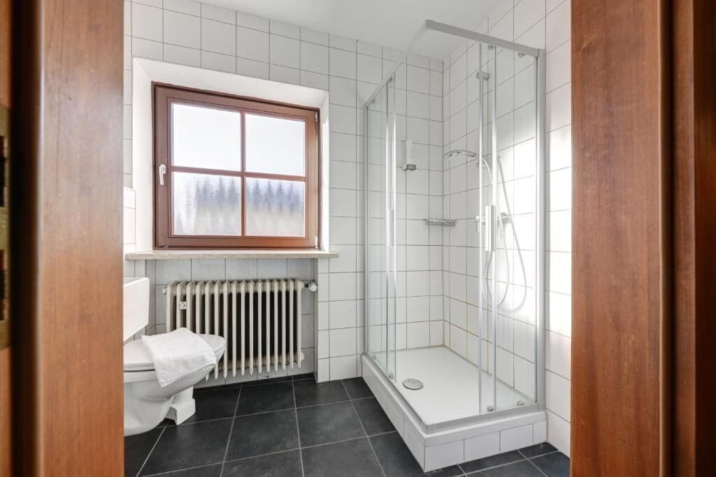 A bathroom with a toilet, a window, a radiator, and a glass-enclosed shower.