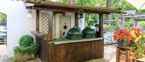 A rustic outdoor bar area with a wooden counter, green planters, and a canopy.