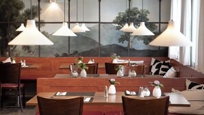 A restaurant with wooden tables and benches, hanging pendant lights, and a mural of trees on the wall. - Weichandhof (Munich)