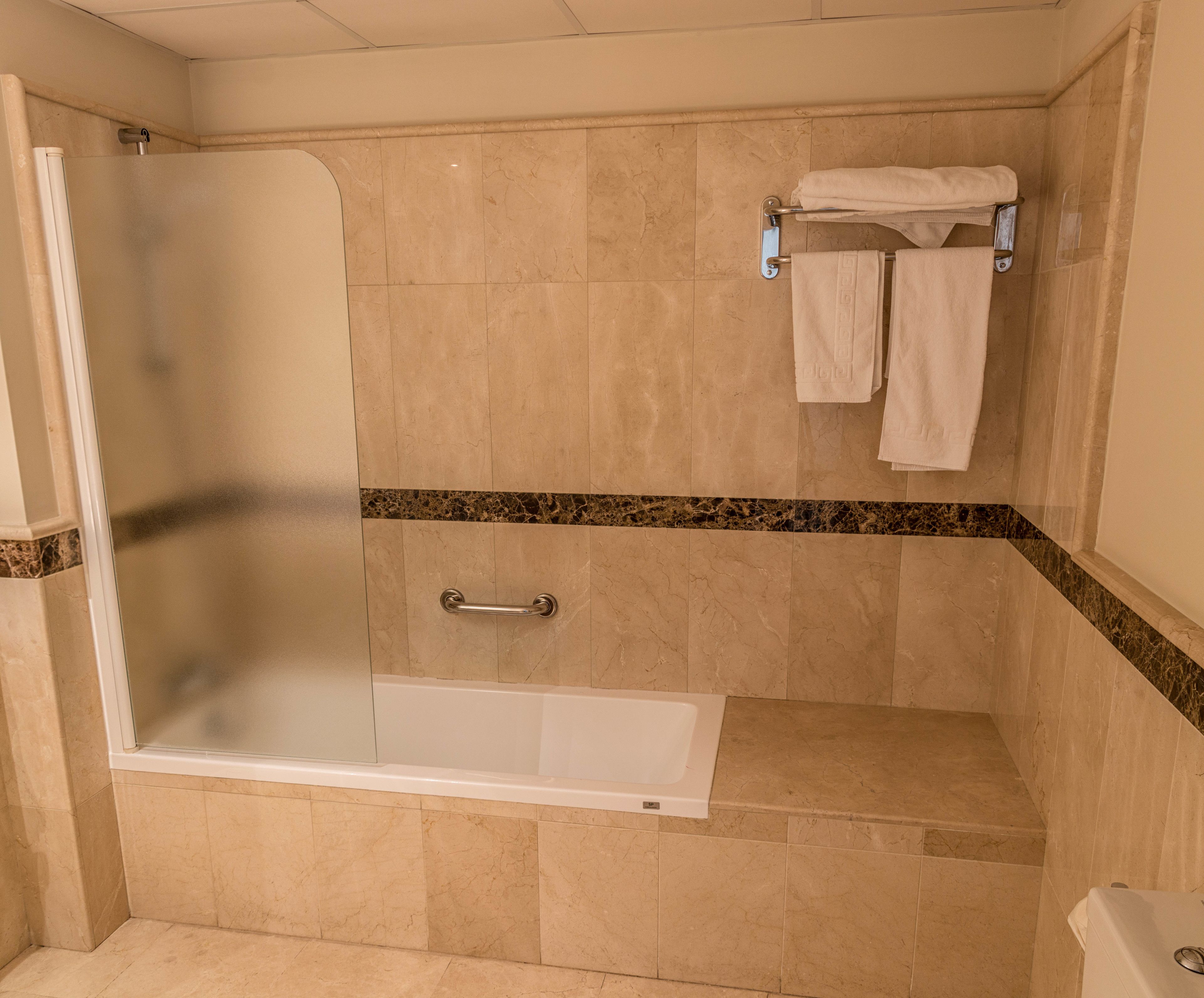 A bathroom with a glass-enclosed shower, a bathtub, and a towel rack with towels.