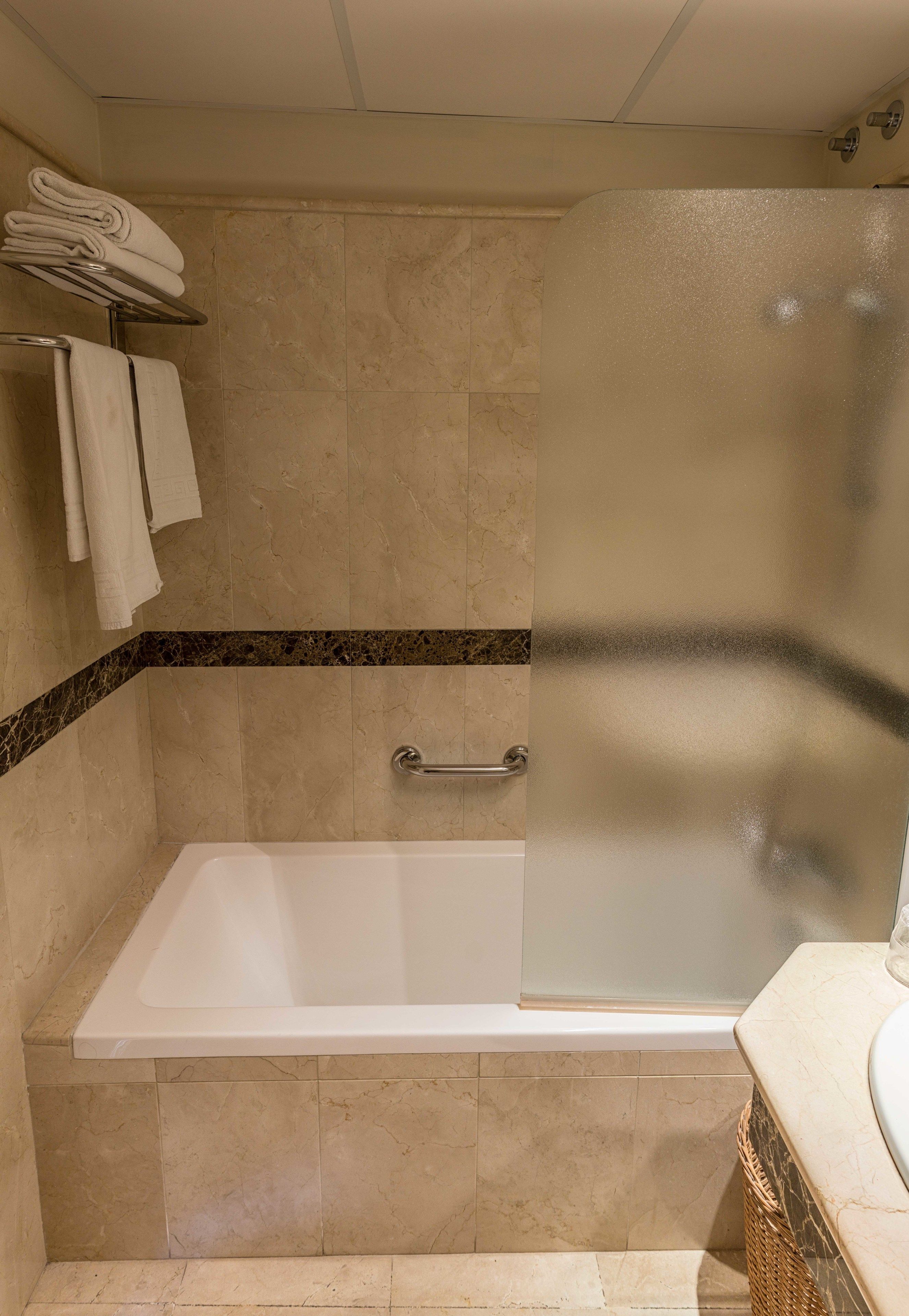 Un baño con bañera, cabina de ducha de vidrio y un perchero con toallas dobladas.