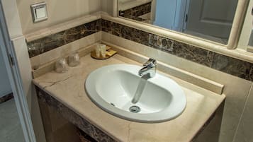 Une salle de bain avec un lavabo blanc, un miroir et un comptoir en marbre.