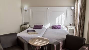 A hotel room with two beds, a small table, two chairs, and a nightstand with a lamp.