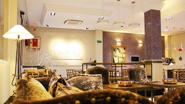 A dining area with tables and chairs, a staircase, and a wall with a painting. - Hotel Sevilla (Ronda)