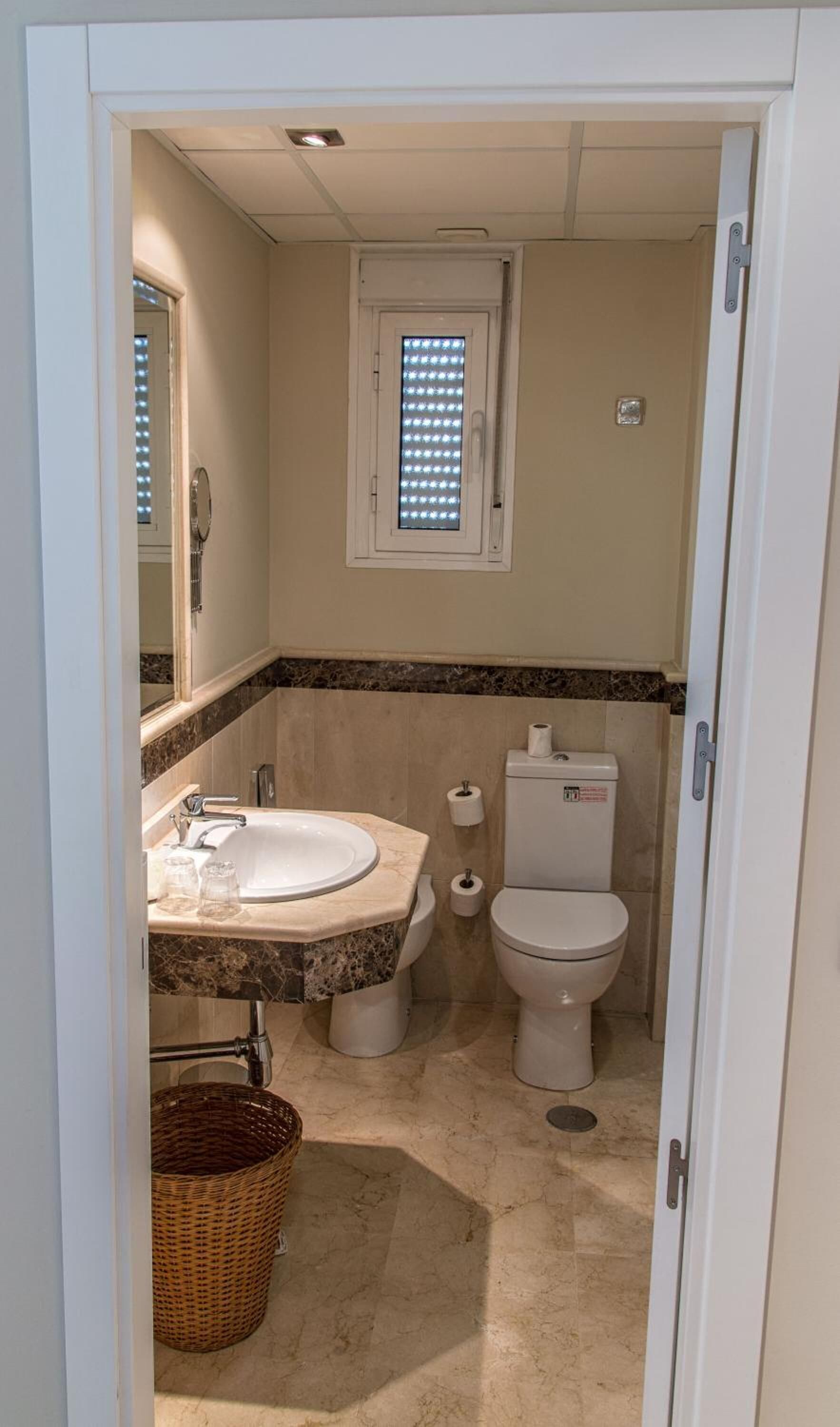 A small bathroom with a sink, toilet, and a window with blinds.