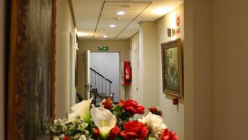Un pasillo de hotel con un arreglo floral grande, un cuadro en la pared y un extintor.