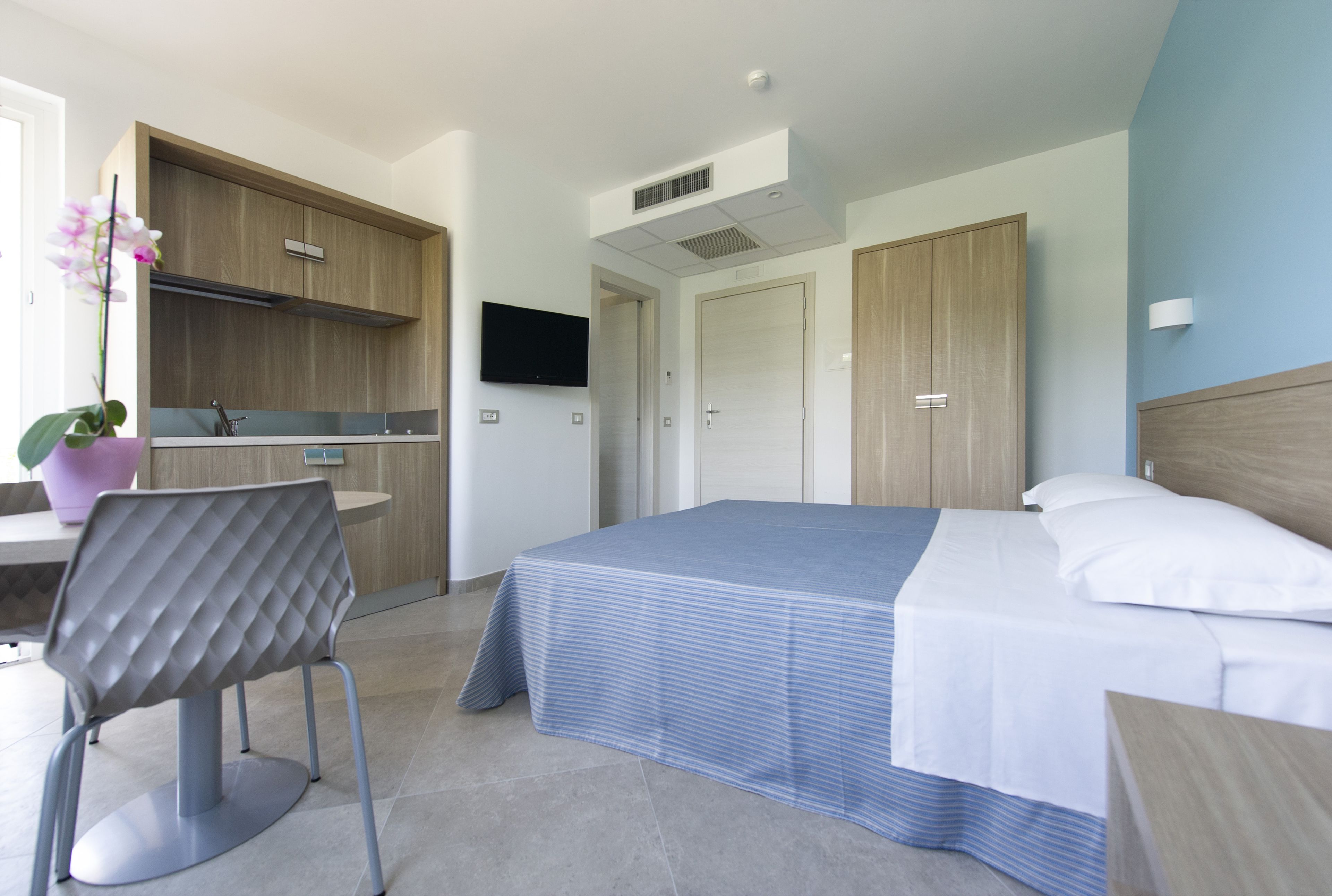 A modern hotel room with a bed, a desk with a chair, a television, and a large wardrobe.