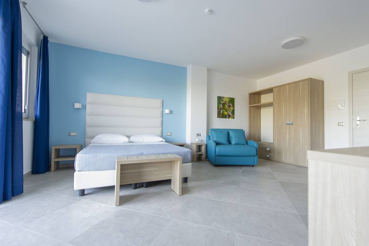 A modern bedroom with a bed, bedside tables, a blue sofa, and a wardrobe.