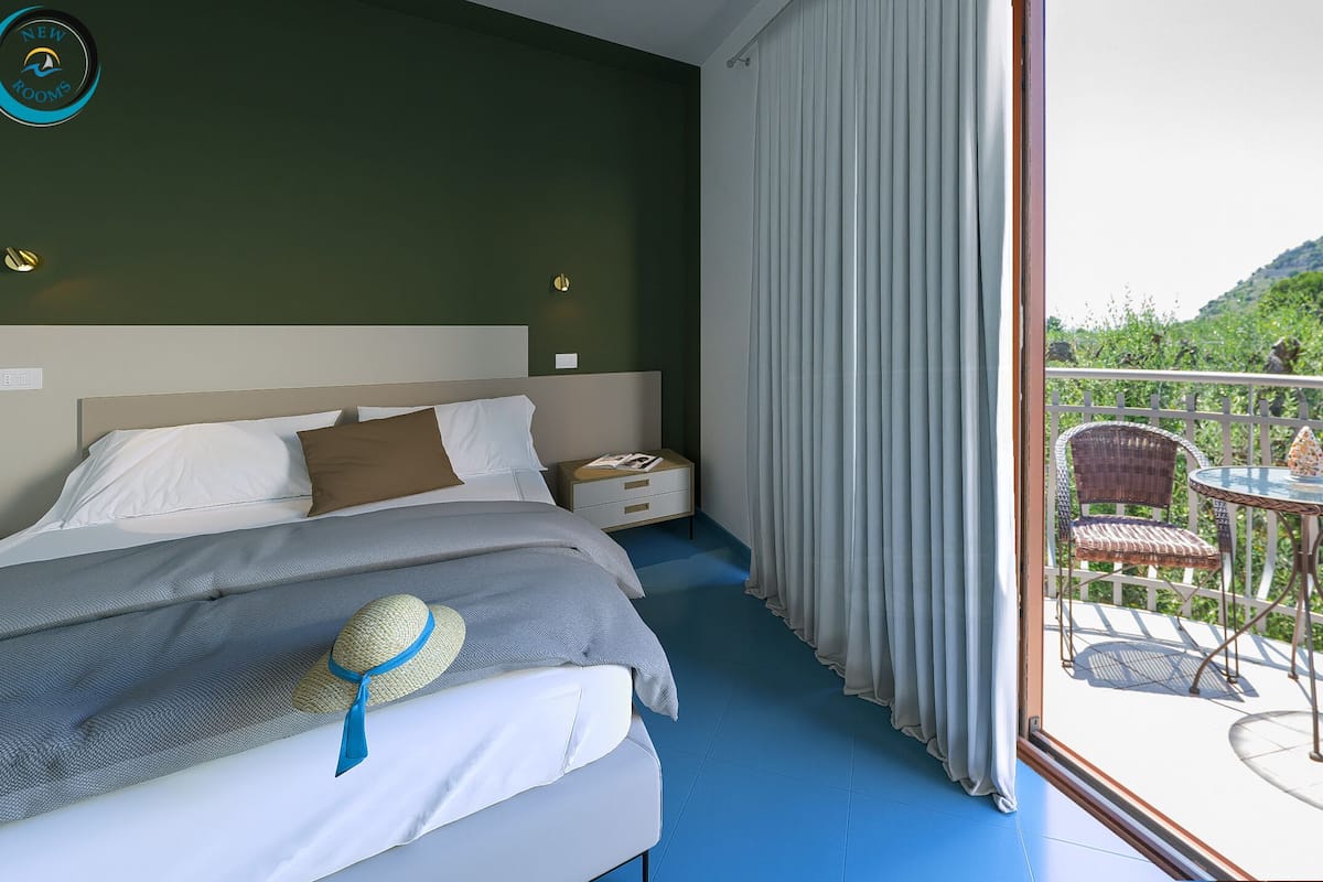 A bedroom with a bed, nightstands, and a view of a balcony with outdoor furniture.