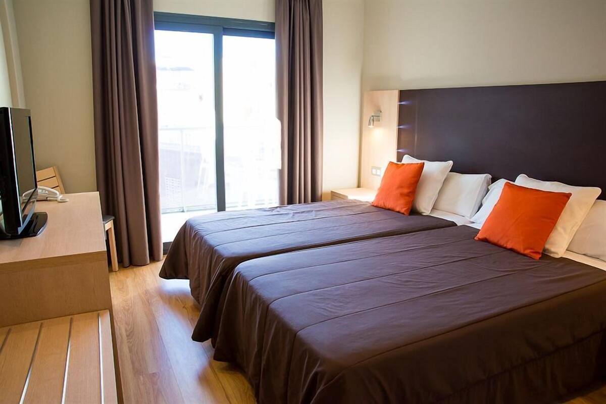 A hotel room with two beds, a TV, and a window with curtains.