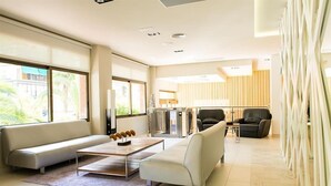 A modern living room with a sofa, coffee table, and chairs. There is a large window providing natural light and a view of the outside. - Hotel Melina (Benidorm)
