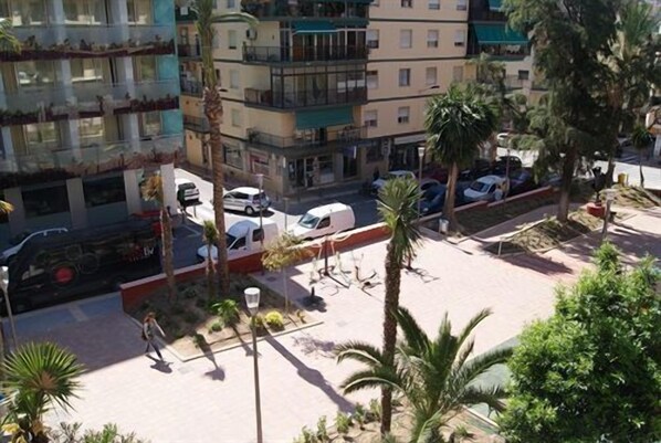 A multi-story residential building with balconies, a parking area with cars, and palm trees. - Hotel Melina (Benidorm)