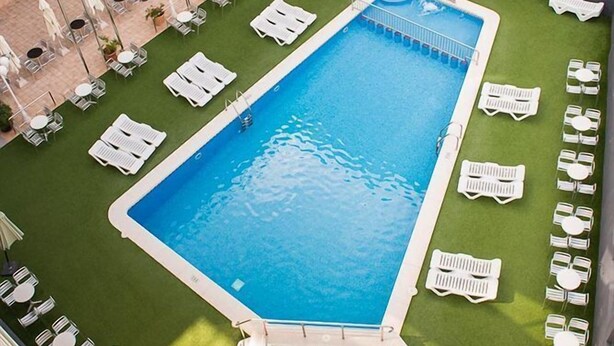 A rooftop pool with a hot tub, surrounded by lounge chairs and tables, and a building with balconies in the background. - Hotel Melina (Benidorm)