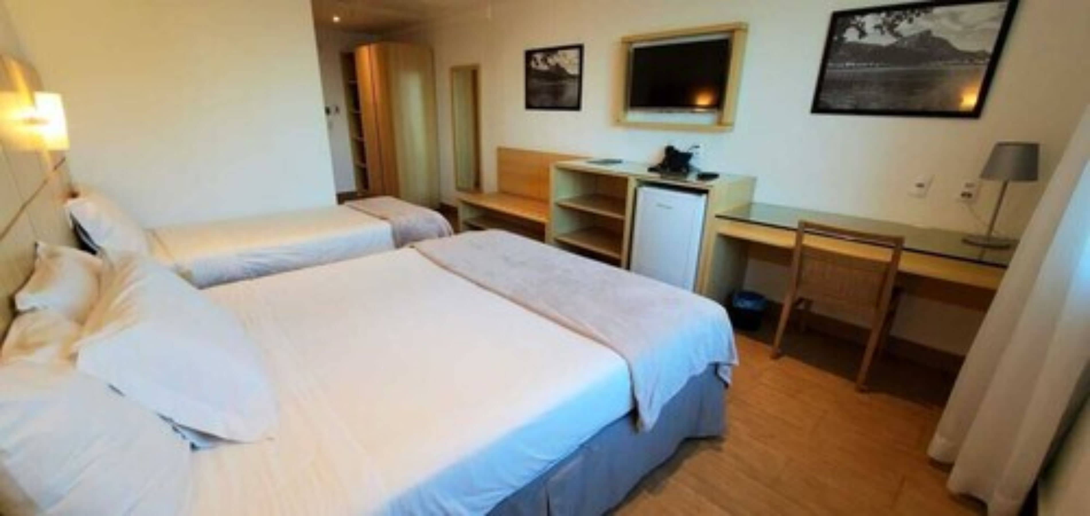 Une chambre d’hôtel avec deux lits, un bureau, un petit réfrigérateur et un miroir.