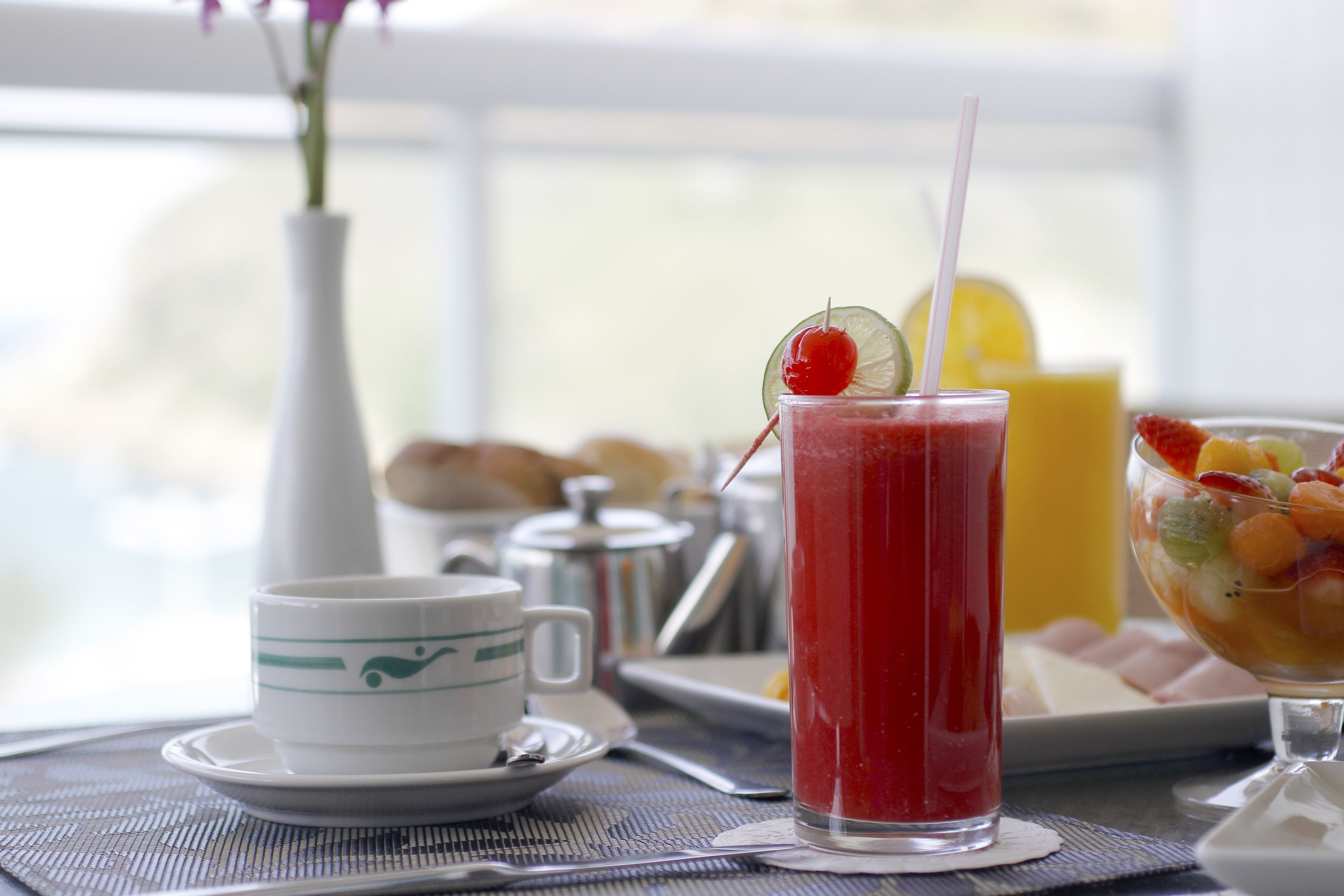 A breakfast setting with a glass of red juice, a cup, and a fruit bowl on a table.