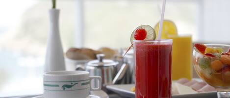 A breakfast setting with a glass of red juice, a cup, and a fruit bowl on a table.