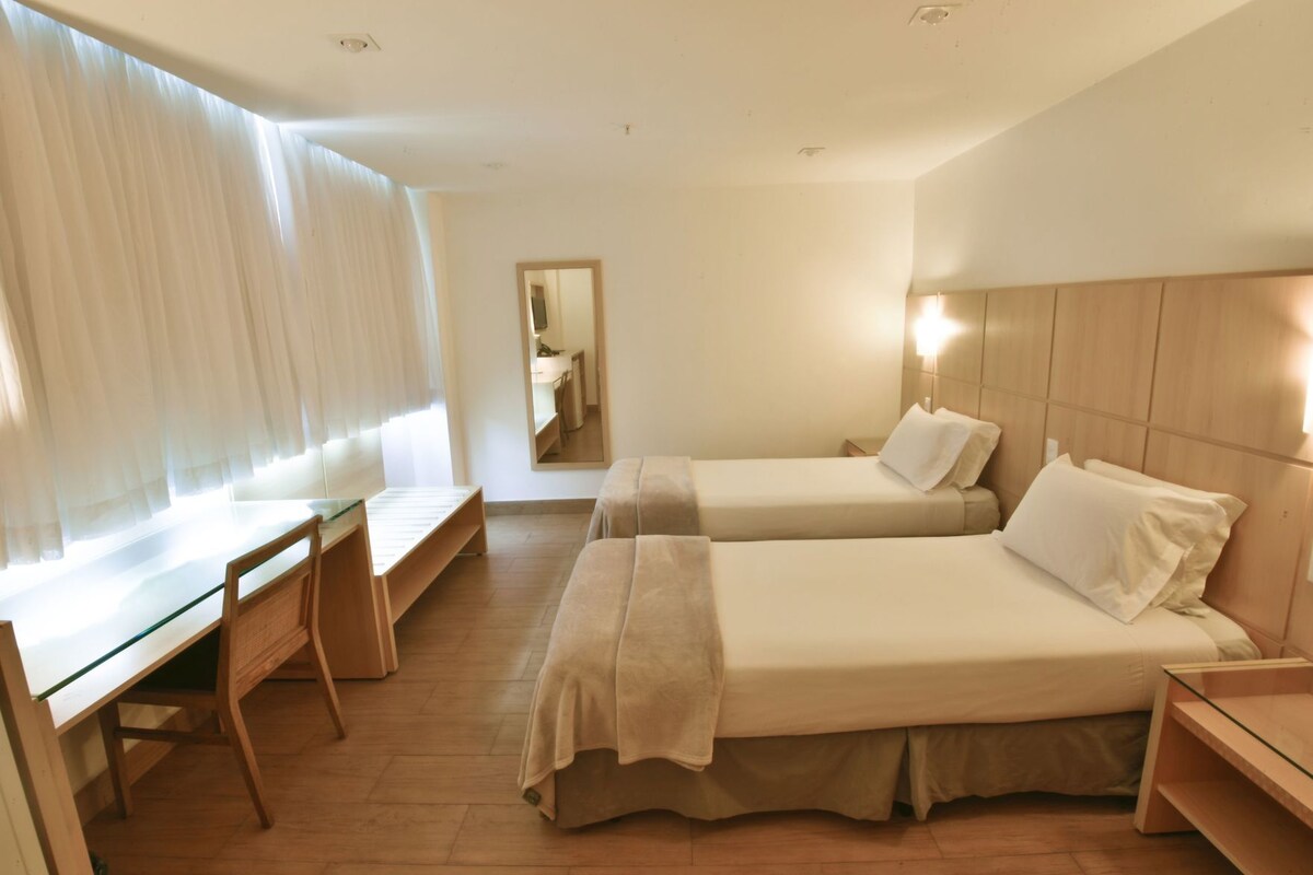 A hotel room with two beds, a desk, and a mirror.