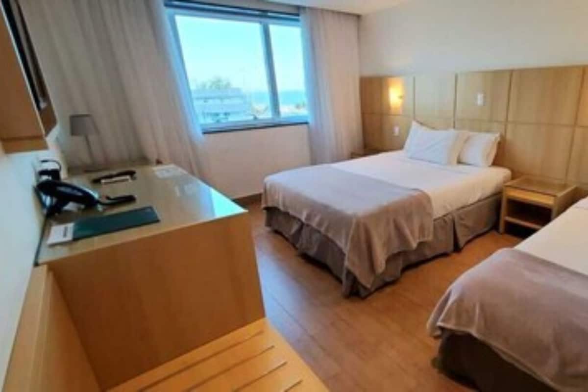 Een hotelkamer met twee bedden, een bureau met telefoon en een raam met gordijnen.