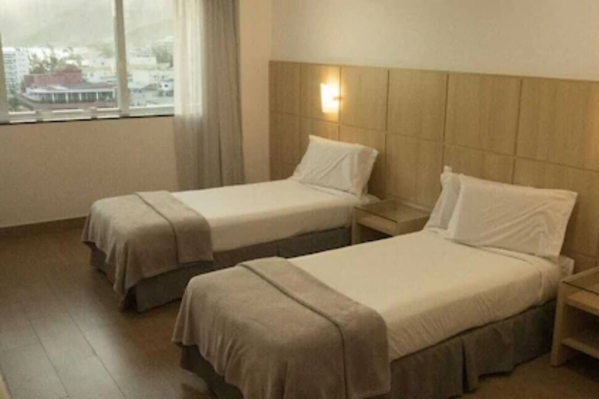 Twee eenpersoonsbedden met hoofdeinden, nachtkastjes en een raam met uitzicht op gebouwen.