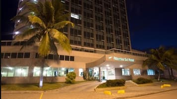 A modern hotel building with a curved facade, palm trees, and a well-lit entrance.