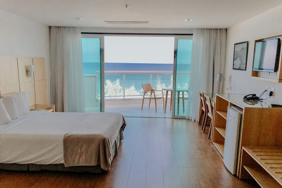 Een hotelkamer met een bed, een bureau, een stoel en uitzicht op de oceaan.