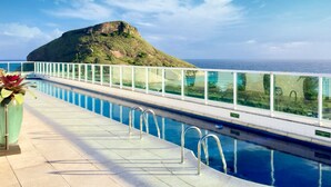 Een zwembad met glazen balustrade met uitzicht op een bergachtig landschap en de oceaan.