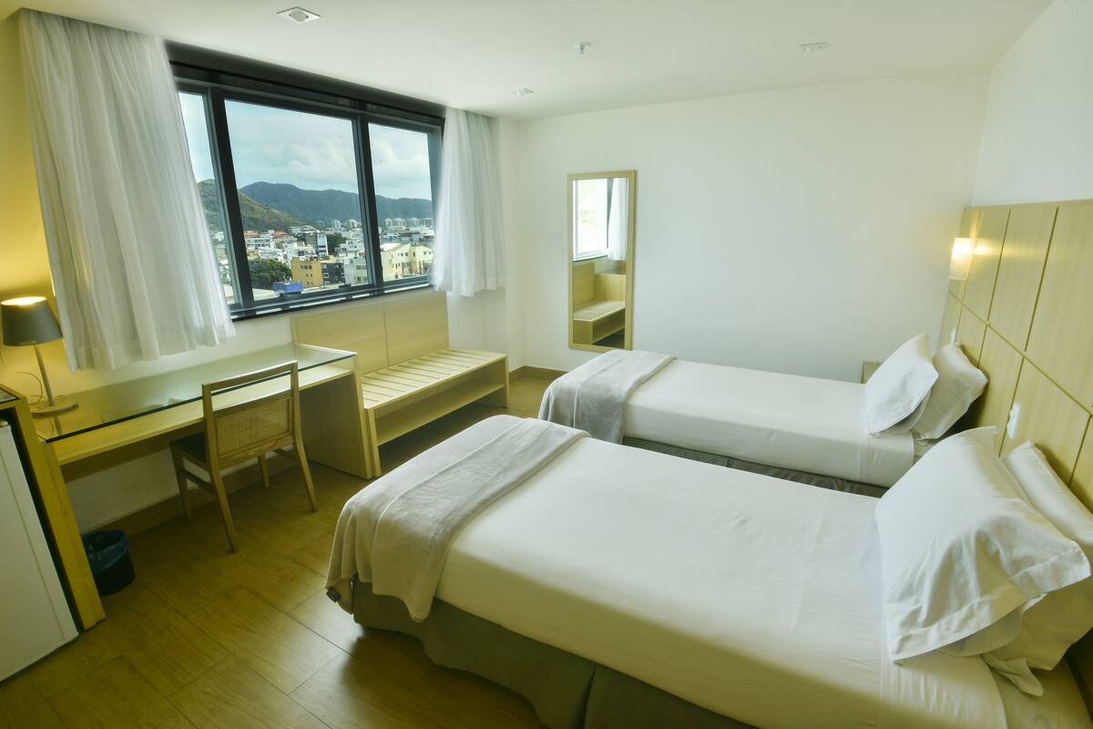 Een hotelkamer met twee bedden, een bureau, een stoel en een raam met uitzicht op de stad.