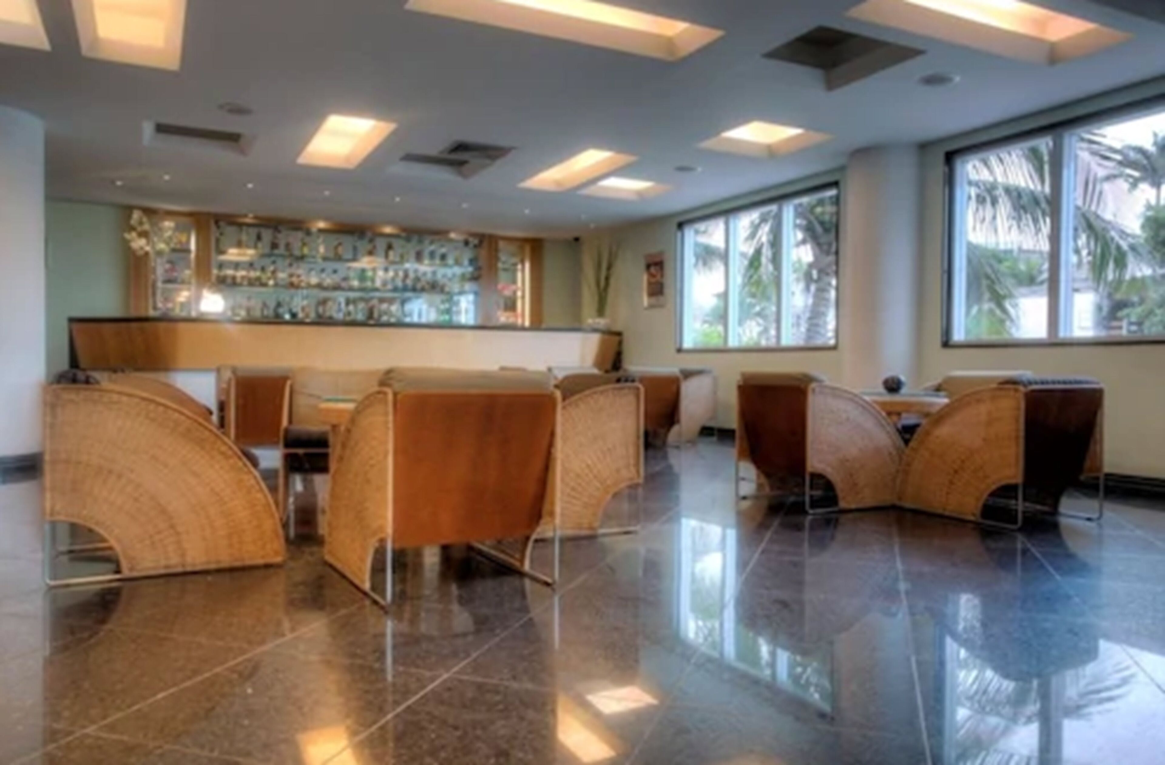 A modern bar area with a polished floor, curved wooden chairs, and a well-lit ceiling with rectangular lights.
