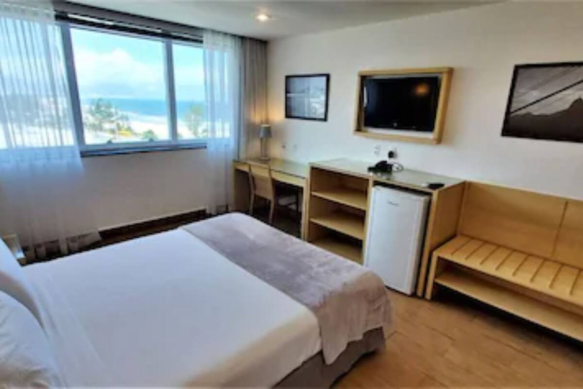 Een hotelkamer met een bed, een bureau, een stoel, een klein tafeltje en uitzicht op de oceaan.