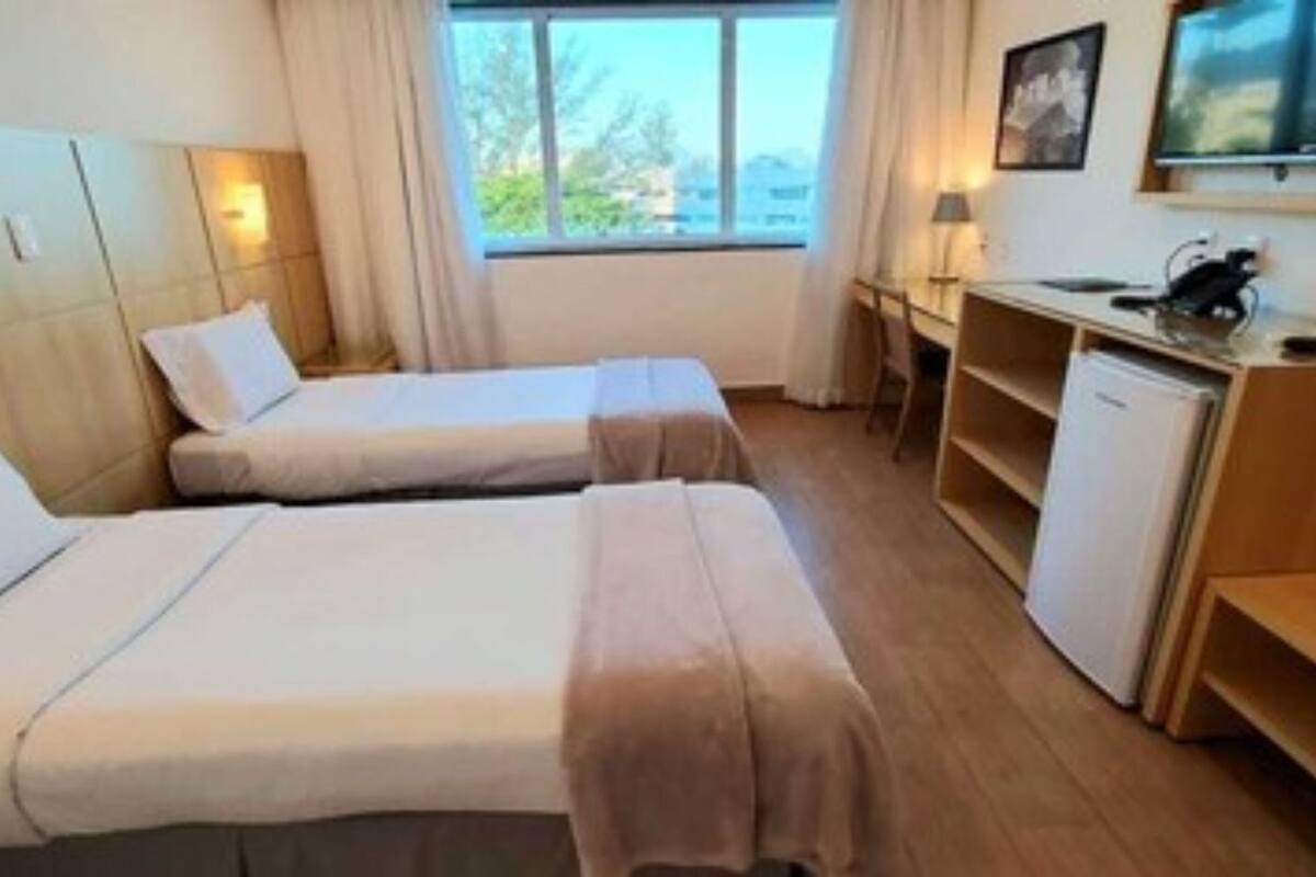 Een hotelkamer met twee bedden, een bureau, een stoel, een kleine koelkast en een raam met uitzicht.
