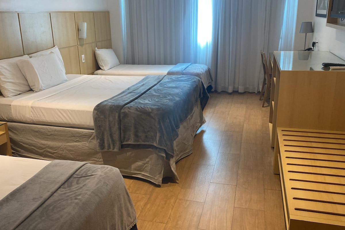 Een hotelkamer met twee bedden, een houten hoofdbord, een nachtkastje, een bureau met stoel en een raam met gordijnen.