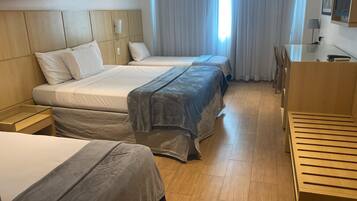 Habitación de hotel con dos camas, cabecero de madera, mesita de noche, escritorio con silla y ventana con cortinas.