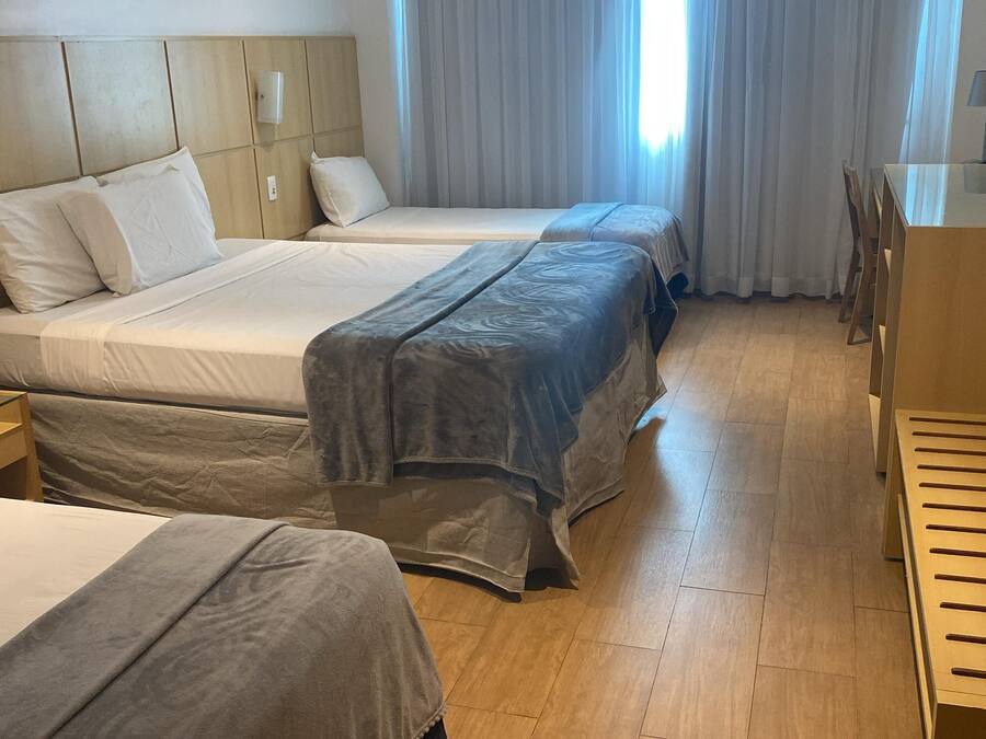 Habitación de hotel con dos camas, cabecero de madera, mesita de noche, escritorio con silla y ventana con cortinas.