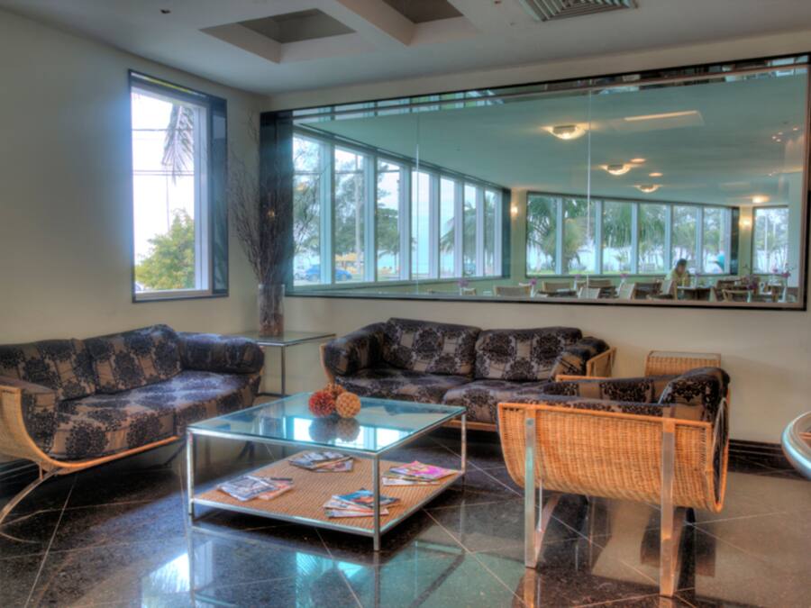 A modern lounge area with a sofa, a glass coffee table, and wicker chairs.