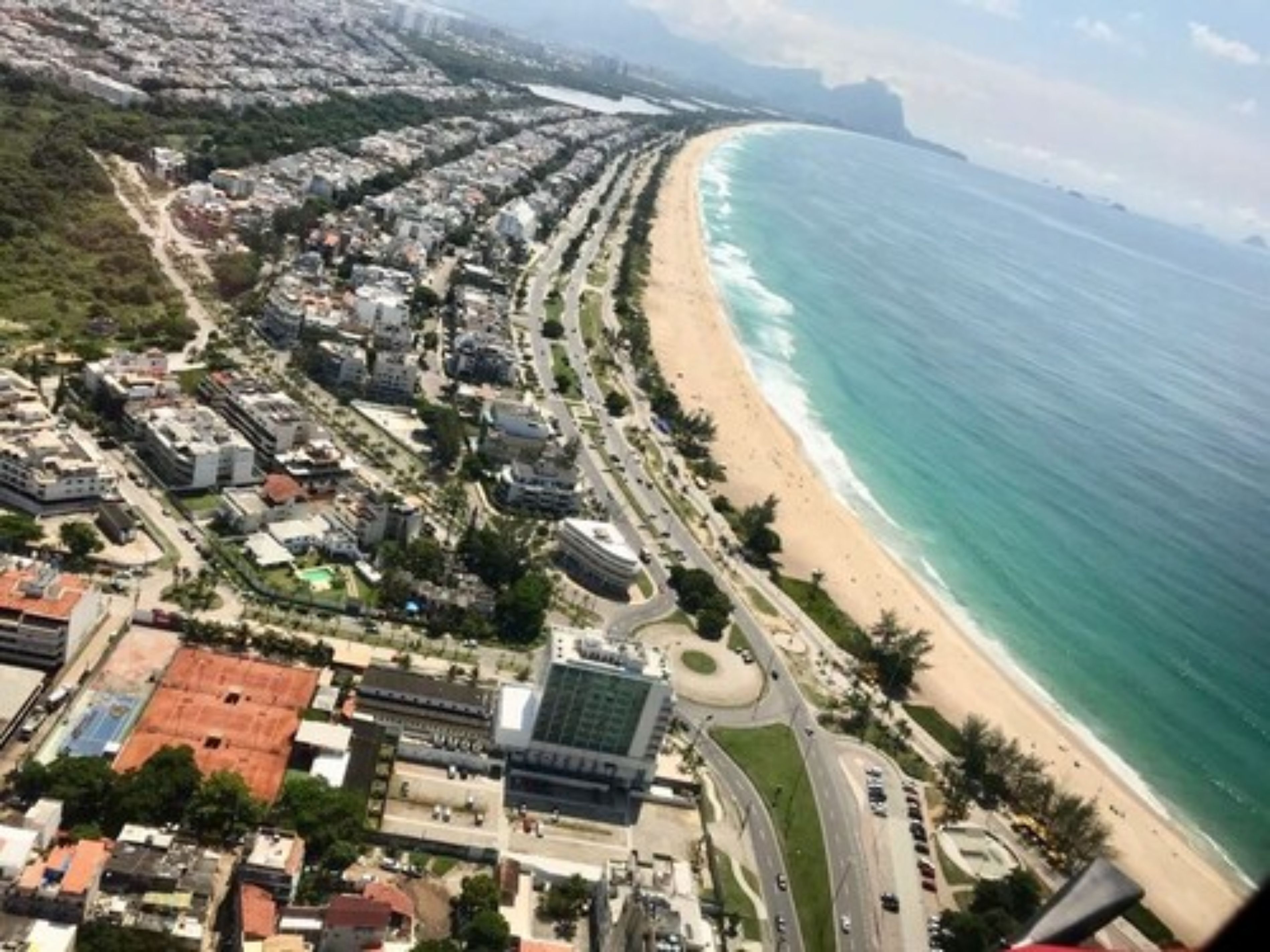 An aerial view of a coastal city with a wide beach, a dense urban area with buildings, and a road leading to the beach.