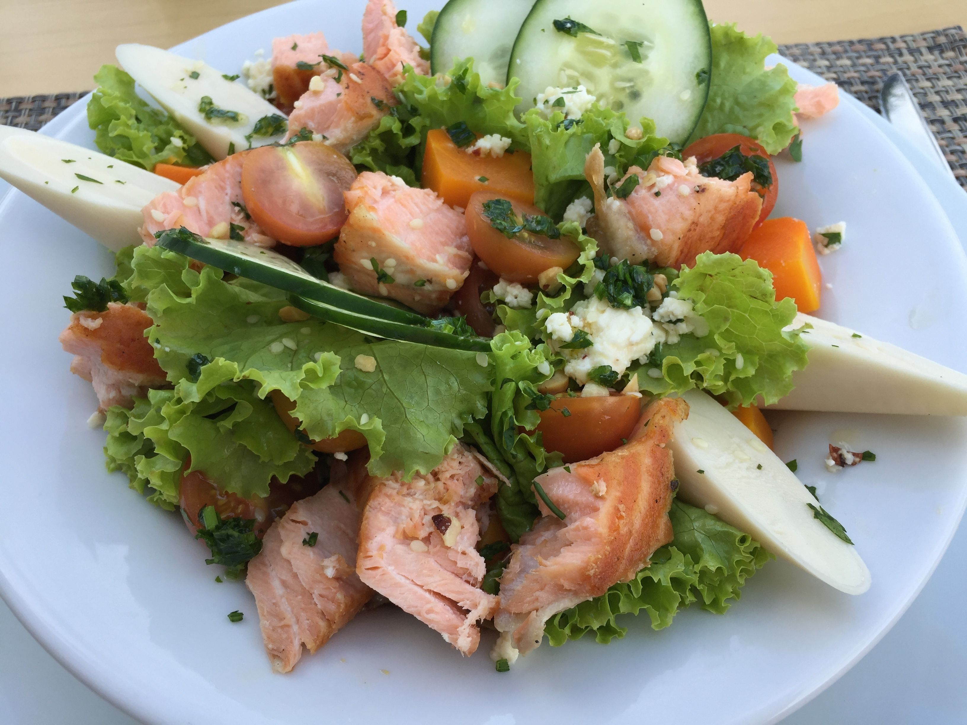 A plate of food with salmon, lettuce, tomatoes, and cheese.