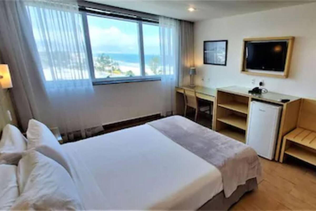 Een hotelkamer met een bed, een bureau, een kleine bank, een raam met uitzicht en een aan de muur bevestigde televisie.
