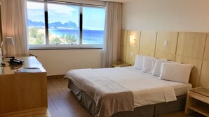 Een hotelkamer met een bed, nachtkastjes, een bureau en uitzicht op zee.