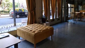 A hotel lobby with a tufted sofa, a dining area with wooden chairs, and large windows with curtains. - Aldeano II (Buenos Aires)
