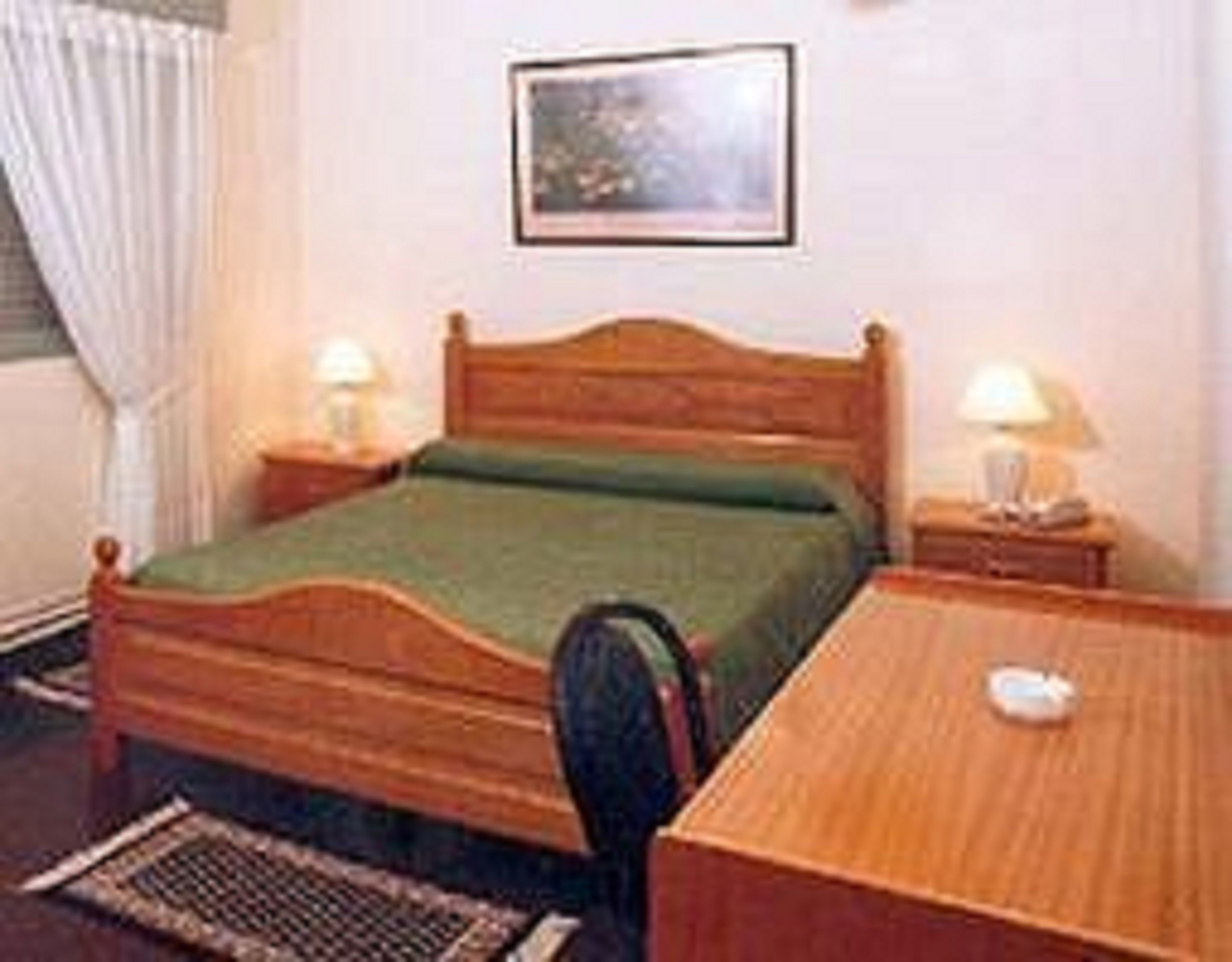 Una cama individual con estructura de madera y ropa de cama verde, flanqueada por dos mesitas de noche con lámparas.