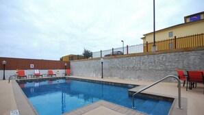 A swimming pool with a stone wall, a metal fence, and red chairs.