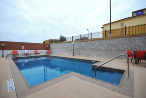 A swimming pool with a stone wall, a metal fence, and red chairs.