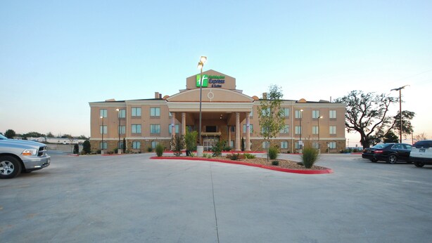 A hotel with a central entrance, multiple windows, and a parking lot.