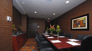 A conference room with a long table, chairs, a kitchenette, and a painting on the wall.