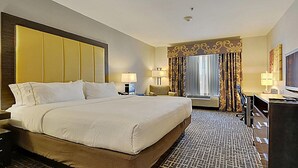 A hotel room with a large bed, two bedside tables, a television, and a window with curtains.