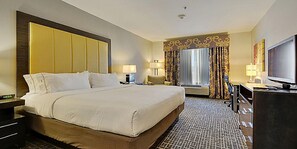 A hotel room with a large bed, two bedside tables, a television, and a window with curtains.